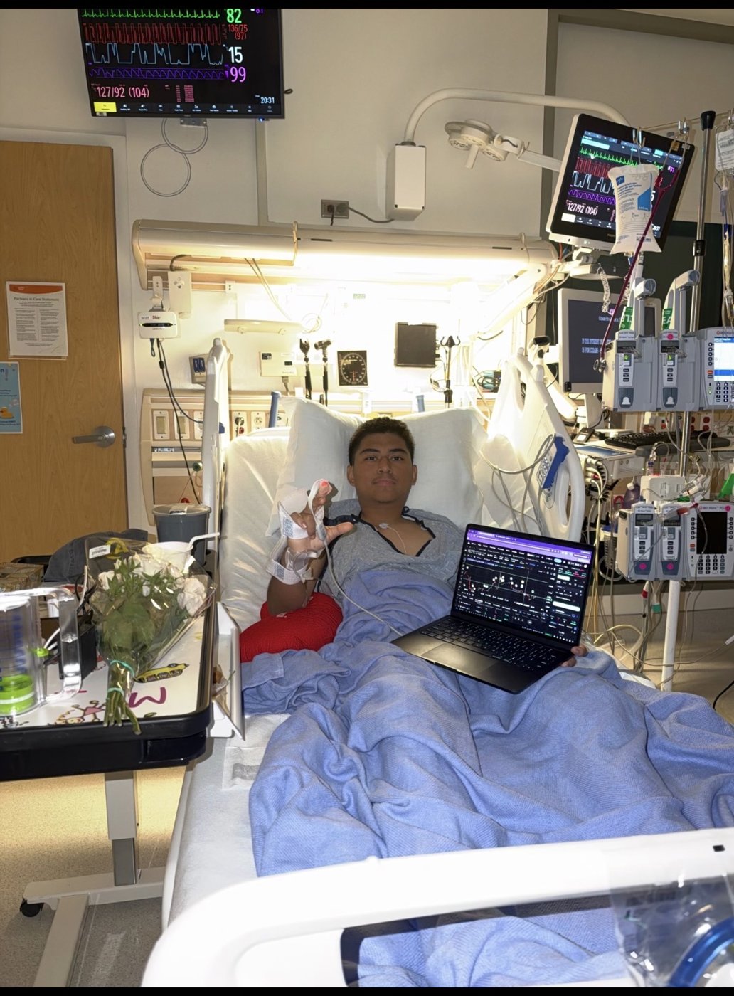 Trenchkid in his hospital bed throwing a peace sign next to a laptop with a chart
